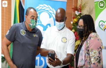 Health and Wellness Minister, Dr. Christopher Tufton (left), and Monitoring and Evaluation Specialist, United Nations Children’s Fund (UNICEF), Donneth Edmondson (right), are given a demonstration of the digitisation of Jamaica’s COVID-19 vaccination card system